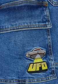 Denim tkanina s izvezenim dizajnom NLO-a u sivoj, bijeloj i žutoj boji, s riječju "NLO" ispisanom debelim žutim slovima.