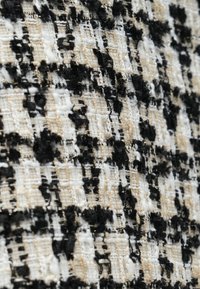 Tekstureret stof i beige, sort og hvid, med et vævet mønster med lodne accenter og diskrete metalliske tråde over det hele.