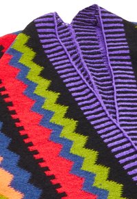 Poncho tricotat multicolor cu modele zigzag în roșu, verde, albastru și galben, având o guleră în dungi mov și un fundal negru.