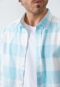 Blau-weißer karierter Button-up-Hemd aus weichem Material, mit einem klassischen Kragen und einem weißen T-Shirt darunter.