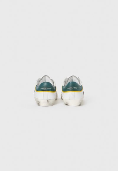 White sneakers with a teal accent at the heel, yellow stripe, and distressed rubber sole. Visible logo on the back.