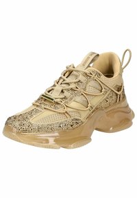 Zapatilla beige con una parte superior de malla texturizada, adornada con rhinestones, y una suela de goma brillante y translúcida. Cuenta con cordones y una lengüeta.