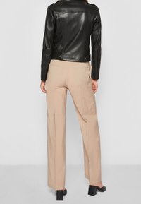 Černá kožená bunda s přiléhavým střihem, doplněná světle béžovými kalhotami s širokými nohavicemi. Oblečení má jednoduchý design a minimální kovové doplňky.