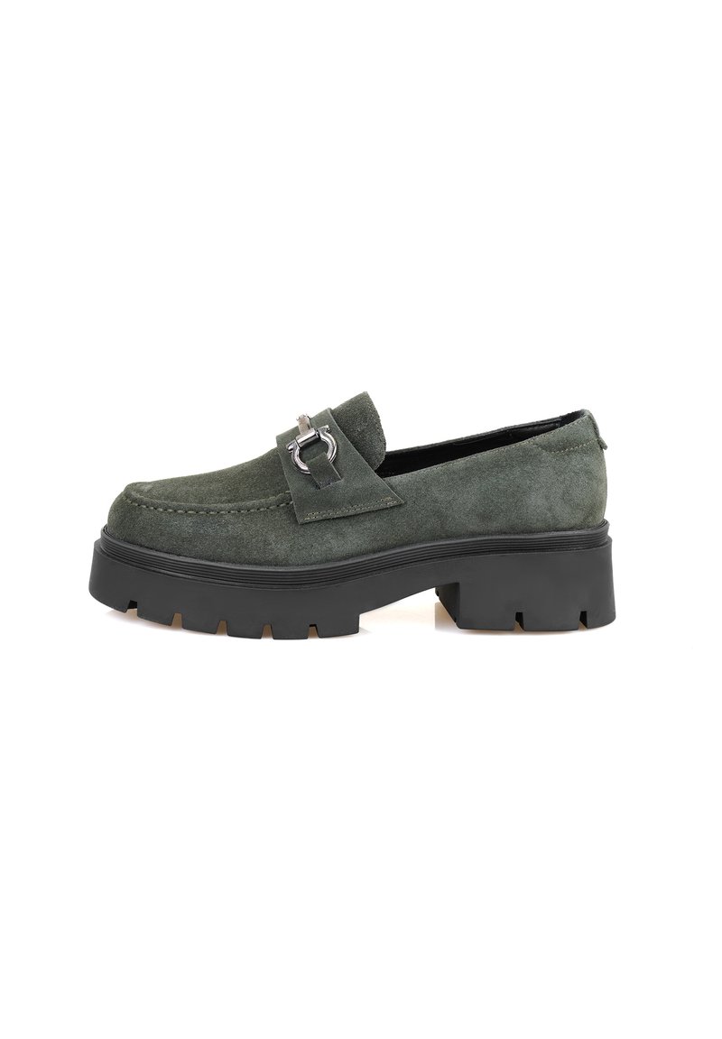 Grüne Wildleder-Slipper mit einer massiven schwarzen Plateausohle und einem dekorativen silbernen Schnallen-Detail auf dem Spann.