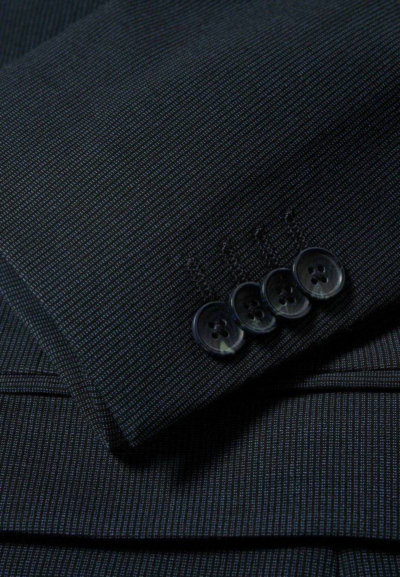 Mörk randig kostymärm med fyra svarta knappar som är prydligt sydda i rad nära manschetten.