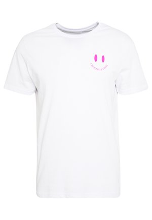 T-shirt blanc à manches courtes avec un petit visage souriant rose et le texte "UNE MEILLEURE VERSION DE MOI ARRIVE" sur le haut gauche de la poitrine.