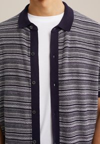 Chemise à boutons avec un col marine et des rayures grises et blanches à motif. Présente une coupe décontractée et une texture de tissu respirant.