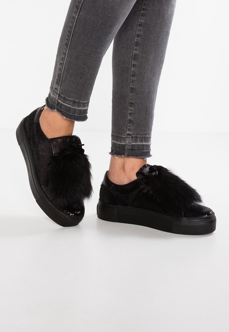 Schwarze Sneakers mit strukturierter Oberfläche, ausgestattet mit einem Überzug aus Kunstfell und einer Schleifenakzent, kombiniert mit grauen cropped Jeans.