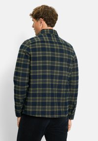 Checkered flannel shirt in navy and olive green. Features a classic collar and buttoned cuffs. Soft texture with a relaxed fit and back yoke.