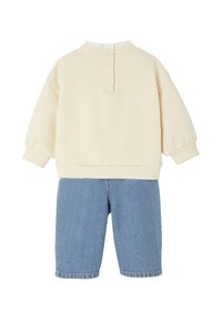 Cremiger Pullover mit geripptem Halsausschnitt und Rückenknöpfen, kombiniert mit blauen Denim-Shorts mit lässiger Passform und umgeschlagenen Säumen.