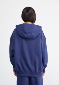 Tmavě modrá oversize mikina z měkké látky. Má prostornou kapuci a žebrované manžety a lemy. Jednoduchý design bez dalších ozdob.