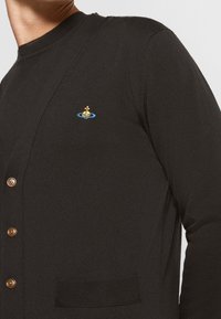 Svart cardigan i strukturerad stickad tyg, med en liten broderad design av segelbåt och bruna knappar framtill.