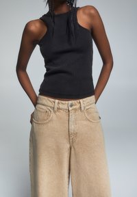 Czarny prążkowany top na ramiączkach zestawiony z jasnobeżowymi szerokimi spodniami z kieszeniami z przodu i zapięciem na guzik. Prosty i casualowy strój.