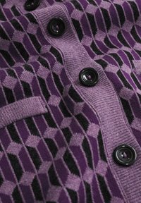 Fialová a černá geometricky vzorovaná pletená látka s černými kulatými knoflíky a žebrovaným okrajem.