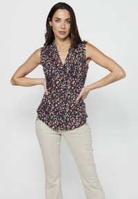 Blusa senza maniche in blu navy con stampa floreale multicolore, con bottoni frontali e delicate rouches sullo scollo, abbinata a pantaloni beige chiaro.