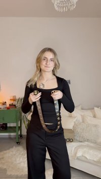 Large ceinture noire avec des clous métalliques tenue par une personne. Caractérisée par une boucle rectangulaire, une texture en cuir lisse et un design minimaliste.