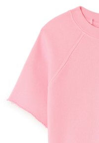 T-shirt en coton rose avec un col rond, des manches raglan courtes et un ourlet légèrement effiloché, avec une texture lisse et une couleur unie.
