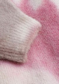 Tissu tricoté doux avec un motif dégradé dans des teintes de rose et de blanc, montrant une texture détaillée et du flou.