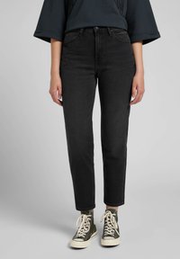 Black high-waisted jeans with a straight fit, four pockets, and a zip fly. Paired with green canvas high-top sneakers.