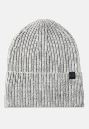Bonnet en maille côtelée gris clair avec revers plié et petite étiquette carrée noire présentant un logo discret "ck" sur le revers.
