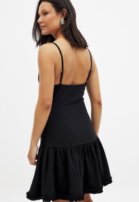 Vestido negro sin mangas con un corsé ajustado y una falda acampanada con volantes. Cuenta con tirantes ajustables y una textura suave.