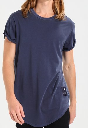 Marineblaue Baumwoll-T-Shirt mit kurzen umgeschlagenen Ärmeln und einem abgerundeten Saum, versehen mit einem kleinen Stoffetikett an der Unterseite.