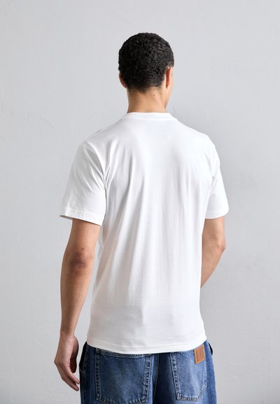 T-shirt en coton blanc à manches courtes et col rond, présentant une texture lisse et une coupe décontractée, porté avec un short en denim bleu.