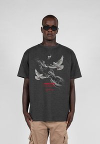 Kulkgrå bomulds t-shirt med et grafisk motiv af to hvide duer og kæder, med ordet "FREEDOM" i rødt under designet.