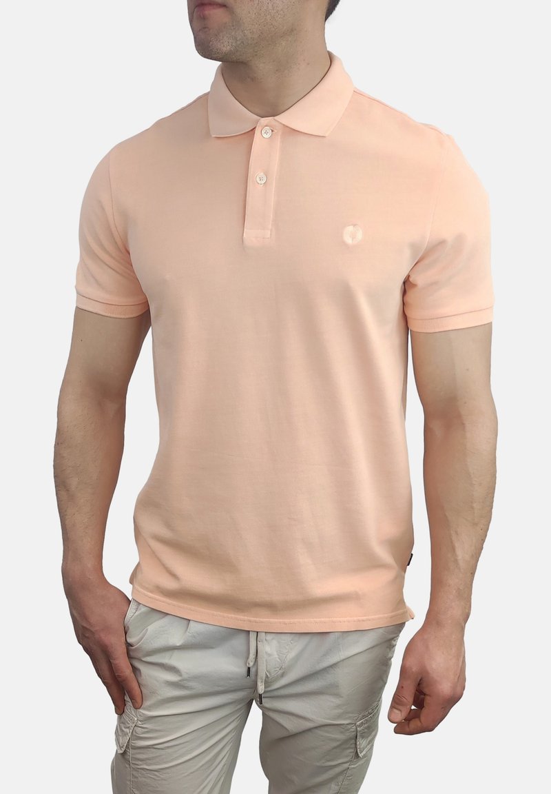 Camisa polo de melocotón con cuello clásico, mangas cortas y un logotipo sutil en el pecho. La tela parece suave y liviana.