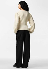 Kremfarvet strikket sweater med ballonærmer, tætsiddende talje, kombineret med sorte viddebukser med nålestriber. Flade sko fuldender outfittet.