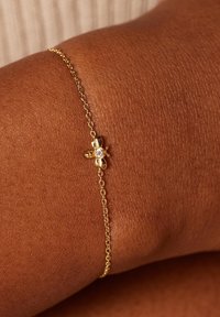 Gouden schakelarmband met een kleine bijcharme, voorzien van een heldere edelsteen in het midden, en toont een verfijnd en gestructureerd ontwerp.