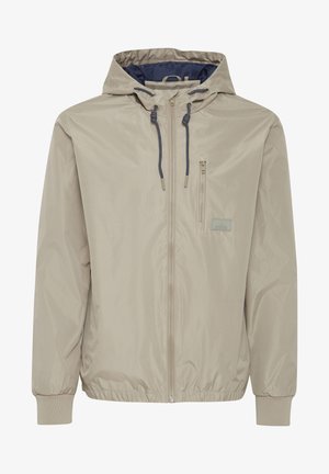 Jasno beżowa kurtka zapinana na zamek błyskawiczny z kapturem, elastycznymi mankietami oraz kieszenią na piersi z prostokątną naszywką logo. Gładki, wodoodporny materiał.