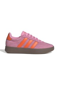 Rosa mocka Adidas-sneakers med orangea ränder och häldetalj, brun sula och snören, visad från sidan på en vit bakgrund.