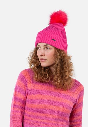 Bonnet en tricot rose vif avec un pompon en fourrure rose sur le dessus et un design côtelé. Porté avec un pull à manches longues rayé rose et orange.