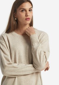 Beige, weicher Pullover mit rundem Hals und gerippten Bündchen, der einen lässigen Schnitt und eine leichte Strickmuster aufweist.