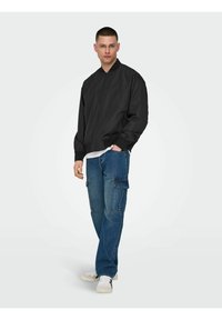 Black bomber jacket with a zip front, ribbed collar, and cuffs, paired with denim cargo pants featuring side pockets and loose fit.