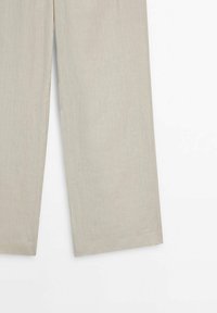 Pantalon beige à jambes droites avec une texture subtile, présenté de la moitié de la cuisse à l'ourlet sur un fond blanc.