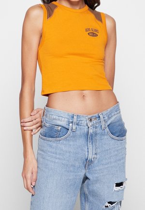 Orange cropped tank top with brown shoulder accents and logo, paired with light blue distressed jeans featuring rips and a faded finish.
