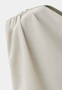 Gros plan d'un tissu beige clair avec une couture élastique froncée sur le bord supérieur, créant de petites plis et une texture.