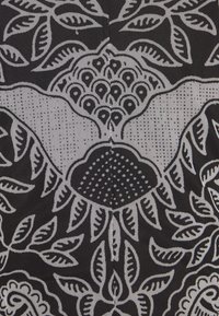 Motif de tissu en noir et blanc avec des feuilles stylisées, des fleurs et des formes abstraites disposées dans un design symétrique.