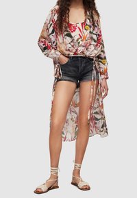 Květinová lehká blůza s dlouhými rukávy, uvázaná v pase, kombinovaná s prodřenými denimovými šortkami. Nosená s sandály na tenkých páscích.