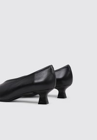 Zapatos de tacón negro de piel con puntera redondeada, tacones cortos y acampanados, y una textura suave. Diseño minimalista sin patrones ni herrajes visibles.