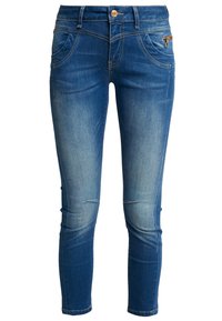Jean en denim bleu à coupe skinny, avec des détails décolorés, cinq poches et un bouton doré. Présente une légère usure au niveau des genoux.