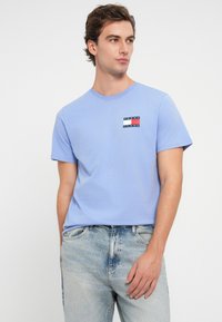 T-shirt de algodão azul claro com mangas curtas e decote redondo. Apresenta um pequeno design de logotipo multicolorido na área do lado esquerdo do peito.