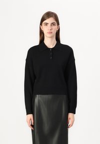 Svart strikket polo genser med krage, front med tre knapper og lange ermer. Kombinert med et svart skinnskjørt. Glatt tekstur generelt.