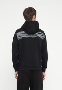 Black hooded sweatshirt with a gray brushstroke design and "NAPAPIJRI geographic" text on the back. Features ribbed cuffs and hem.
