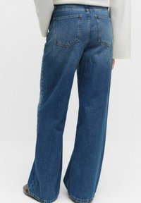 Breda blå jeans i denim med medelhög midja, har två bakfickor och en ren, slät yta.