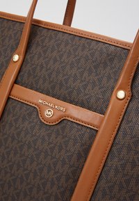 Sac cabas marron Michael Kors avec poignées en cuir et détail logo doré sur tissu monogrammé texturé.