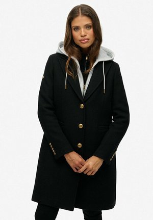 Zwarte wollen jas met een getailleerd ontwerp, gouden knopen, zijzakken en een grijze hoodie eronder. Glad textuur.