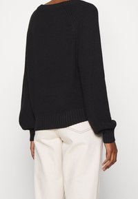 Czarny sweter z dzianiny o luźnym kroju, opadających ramionach oraz ściągaczach przy mankietach i na dole. Teksturowana tkanina dodaje głębi projektowi.
